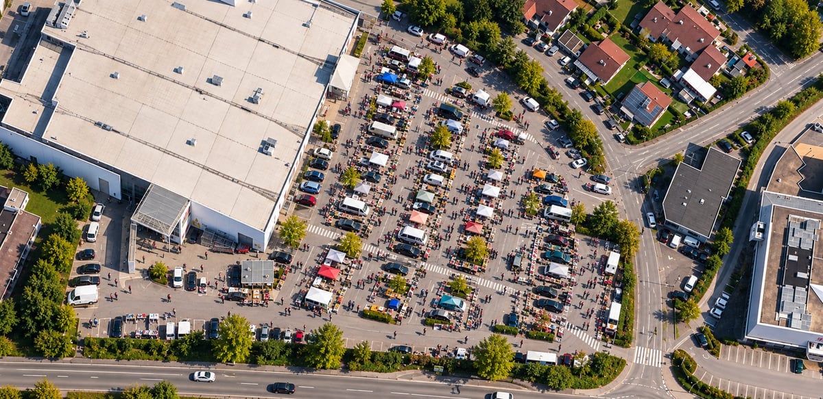 Luftaufnahme vom Parkplatz meinReal (ehemaliger real) in Passau mit geparkten Fahrzeugen, Bäumen und dem umliegenden Gewerbegebiet.